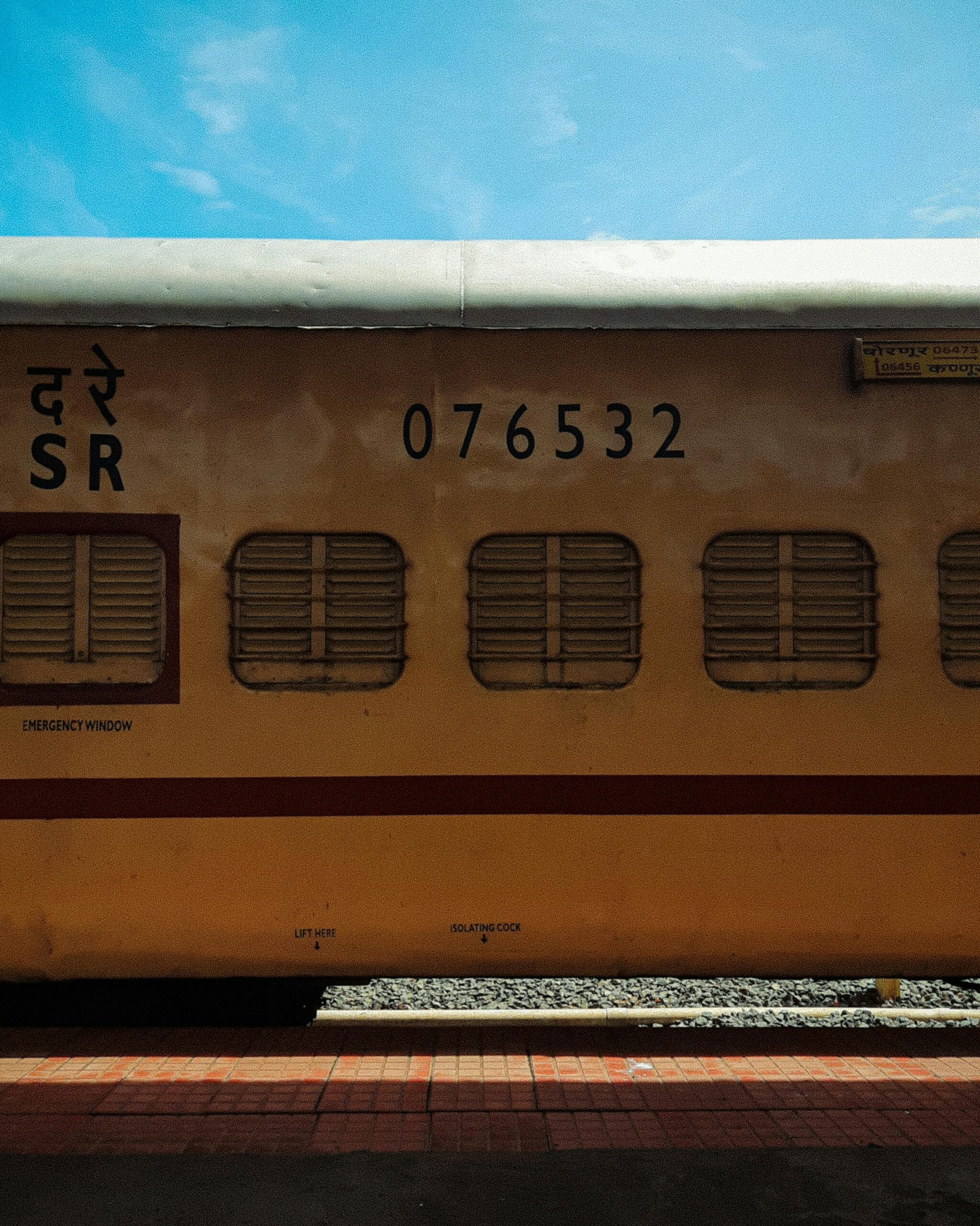 Yellow train carriage at an Indian railway platform under a clear blue sky.